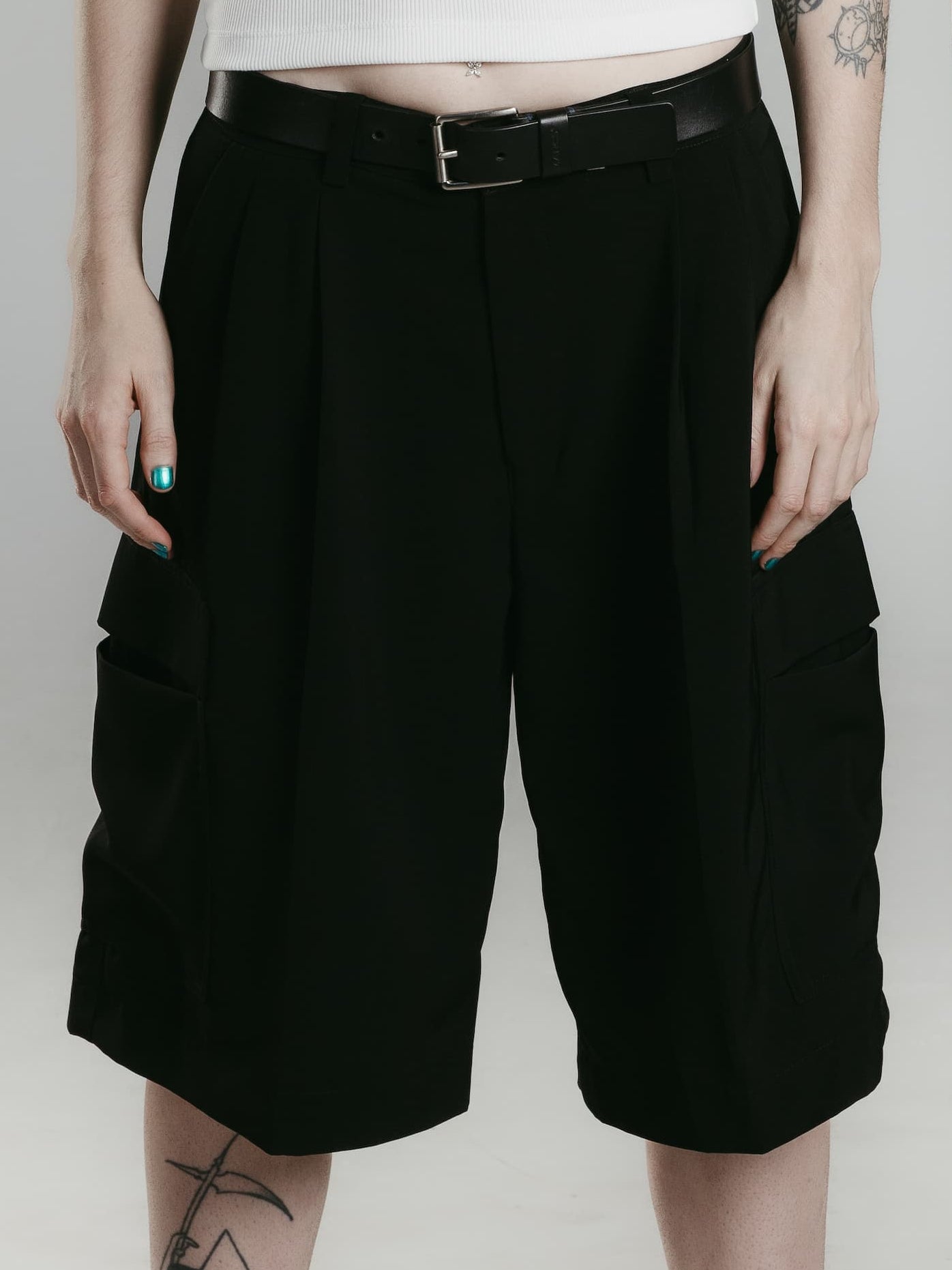 Two models, one wearing black pleated shorts with a white tank top and the other wearing black pleated shorts with a white tank top, standing against a white background.